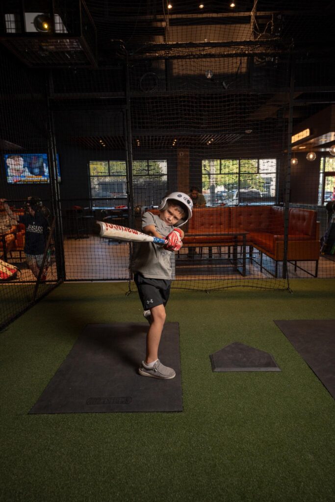 Boy taking a baseball swing and having fun with family at Batbox Dallas indoor sports venue